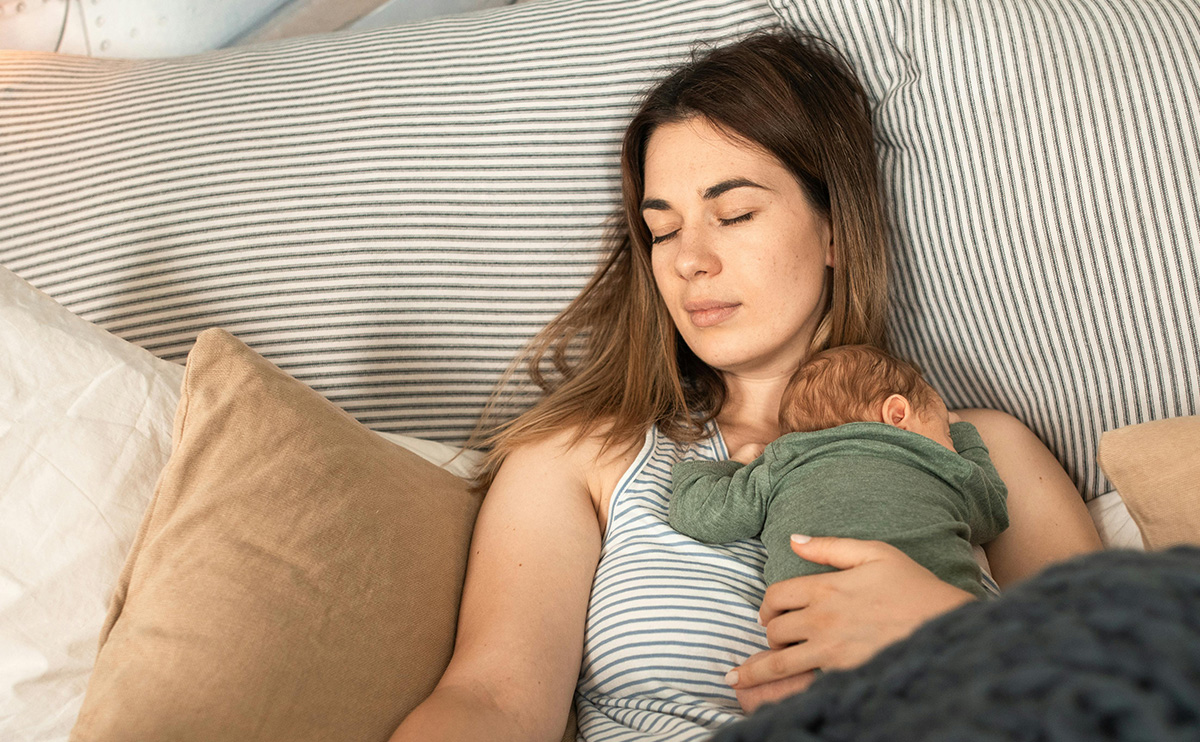 A Woman Resting on the Bed with Her Baby on Top on first week with a newborn