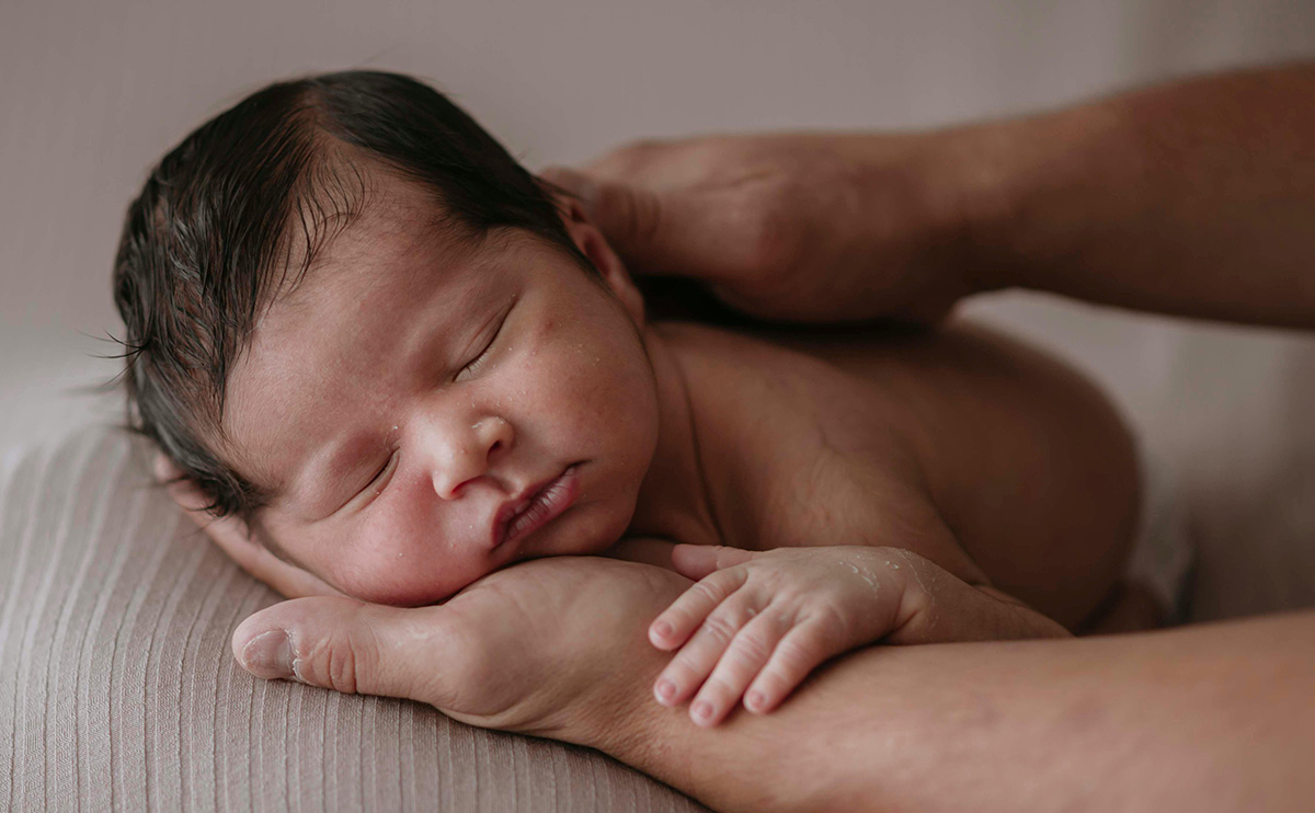 mom gently moisturizing her newborn’s delicate skin in a softly lit nursery, showing calm baby skincare practices